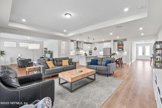 living area with a tray ceiling, french doors, recessed lighting, visible vents, and light wood-type flooring