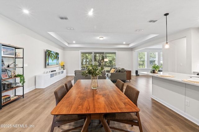 dining space with a tray ceiling, wood finished floors, visible vents, and recessed lighting