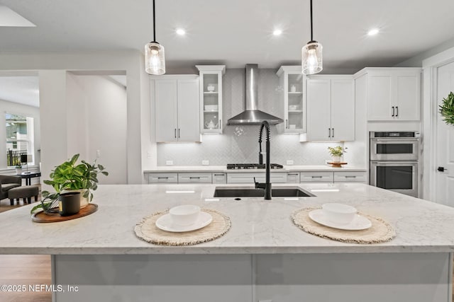 kitchen with white cabinetry, wall chimney exhaust hood, appliances with stainless steel finishes, and decorative light fixtures