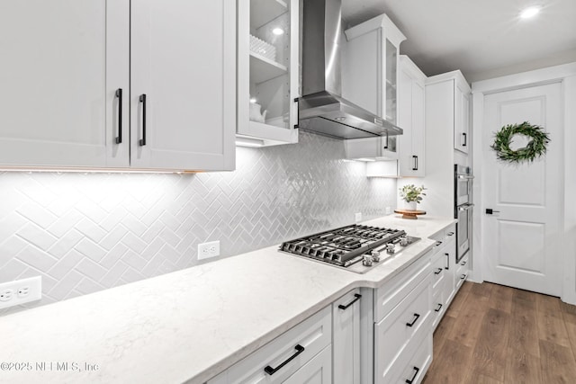 kitchen featuring appliances with stainless steel finishes, dark wood-type flooring, white cabinets, wall chimney range hood, and light stone countertops