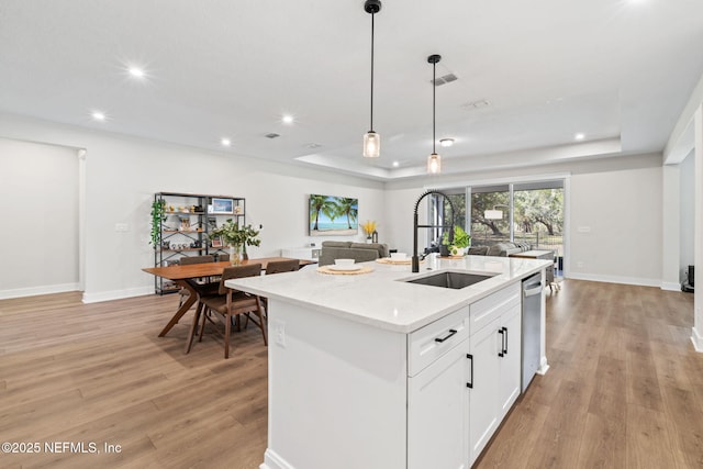 kitchen with a tray ceiling, hanging light fixtures, a sink, and light wood-style flooring