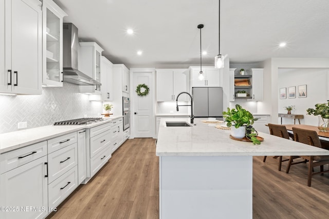 kitchen featuring light wood finished floors, stainless steel appliances, wall chimney range hood, white cabinetry, and a sink