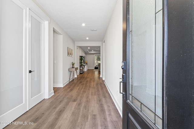 hallway with recessed lighting, a textured ceiling, baseboards, and wood finished floors