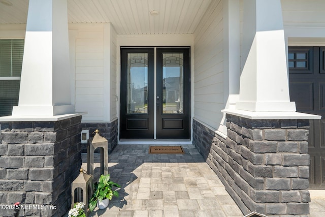 entrance to property featuring stone siding, a porch, and french doors