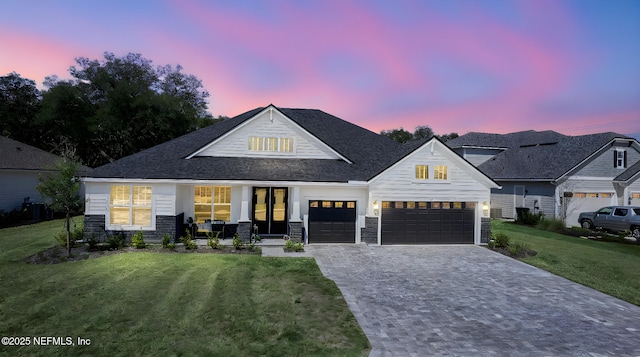 view of front of property featuring an attached garage, stone siding, a front lawn, and decorative driveway