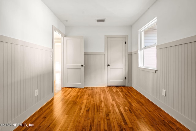 unfurnished bedroom featuring light wood finished floors, wainscoting, and visible vents