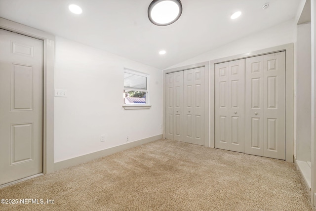 unfurnished bedroom featuring lofted ceiling, light carpet, recessed lighting, and two closets