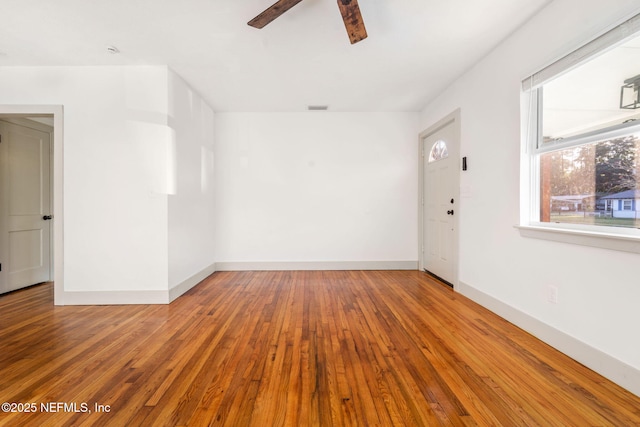 spare room with a ceiling fan, visible vents, baseboards, and wood finished floors