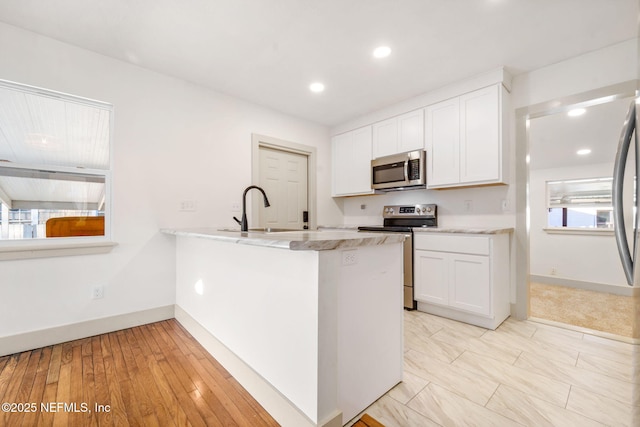 kitchen with light stone counters, stainless steel appliances, a peninsula, a sink, and white cabinetry