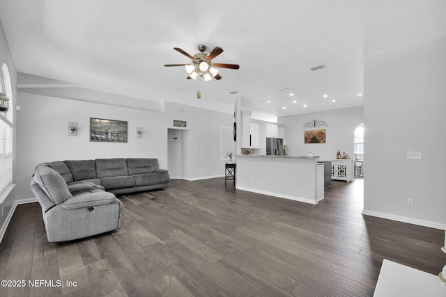 living room featuring a textured ceiling, visible vents, baseboards, a ceiling fan, and dark wood-style floors