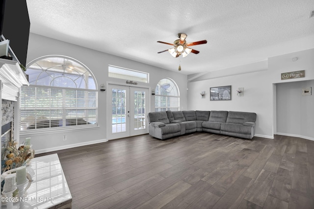 living area with a textured ceiling, dark wood-style flooring, a fireplace, a ceiling fan, and french doors