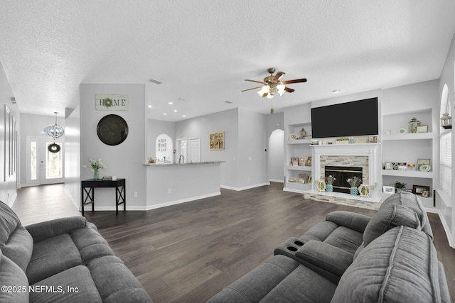 living area featuring dark wood-style flooring, a glass covered fireplace, a textured ceiling, baseboards, and ceiling fan with notable chandelier