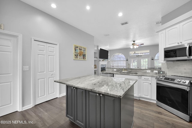 kitchen featuring white cabinets, light stone counters, appliances with stainless steel finishes, a center island, and a sink