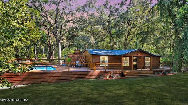 back of property at dusk with an outdoor pool, a deck, and a lawn