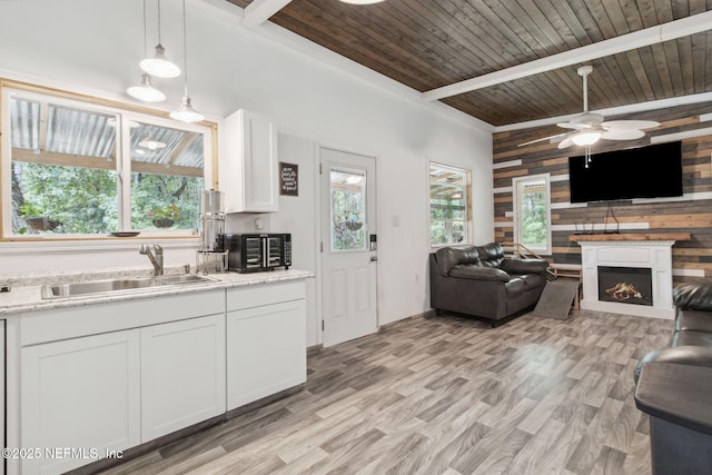 kitchen with open floor plan, white cabinetry, a sink, and wooden walls