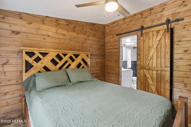 bedroom with a barn door, a ceiling fan, ensuite bath, a textured ceiling, and wood walls