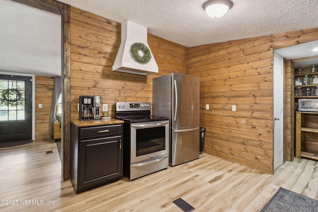 kitchen with premium range hood, appliances with stainless steel finishes, a textured ceiling, and light wood-type flooring