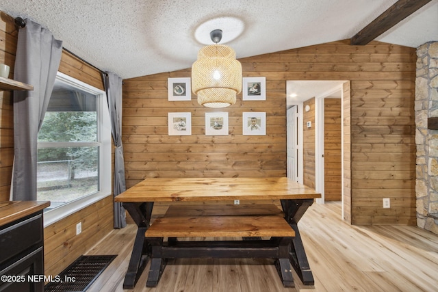 unfurnished dining area with vaulted ceiling with beams, light wood-type flooring, and a textured ceiling