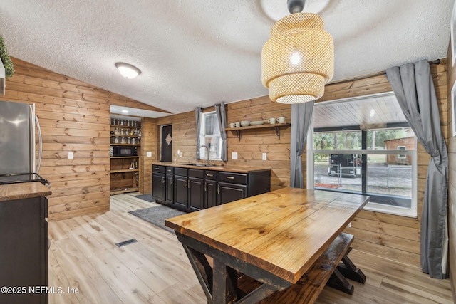 dining room featuring wood walls, a textured ceiling, vaulted ceiling, and light wood-style floors