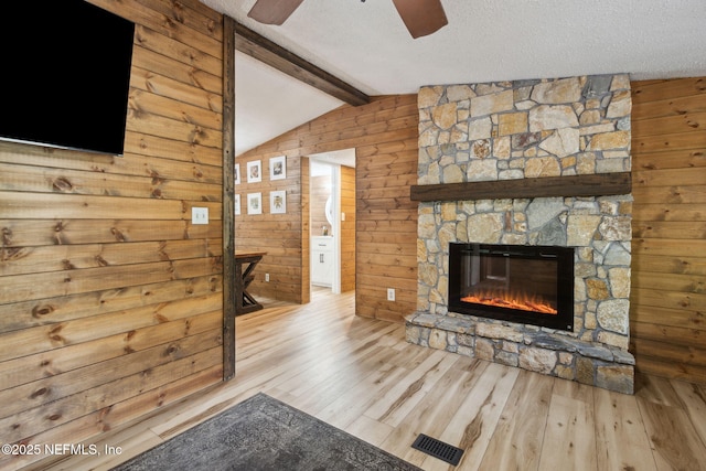 living area featuring lofted ceiling with beams, a stone fireplace, a textured ceiling, and wooden walls