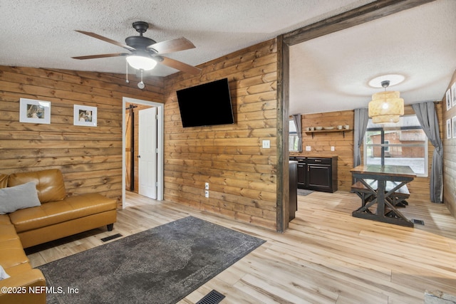 living room with light wood-type flooring, a ceiling fan, visible vents, and a textured ceiling