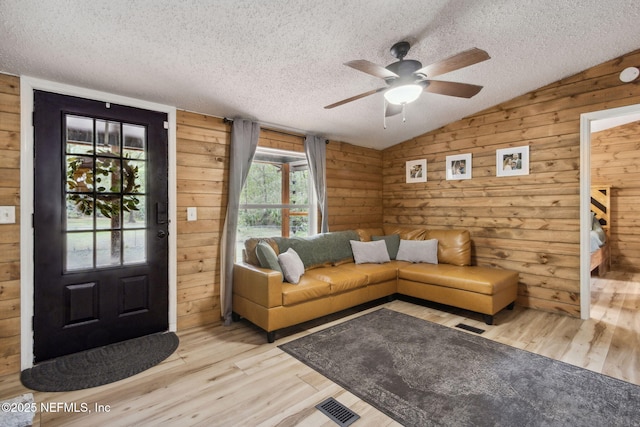 unfurnished living room featuring lofted ceiling, light wood finished floors, and wooden walls