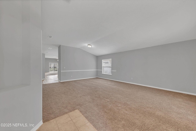 empty room featuring vaulted ceiling, light tile patterned floors, baseboards, and light colored carpet