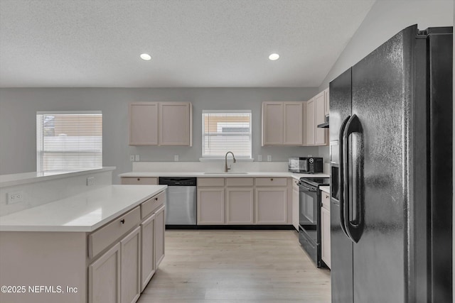 kitchen with light countertops, a textured ceiling, light wood-type flooring, black appliances, and a sink