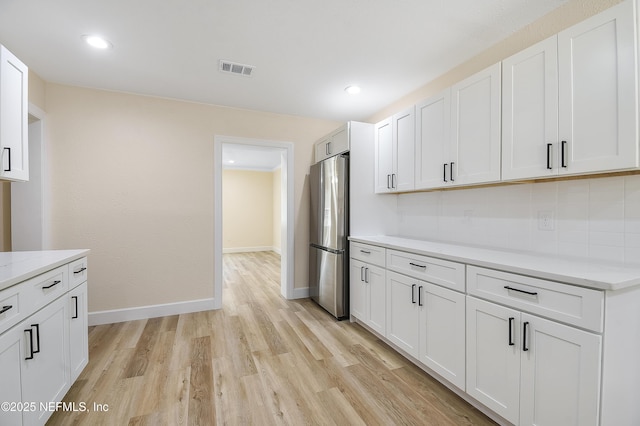 kitchen featuring light wood finished floors, baseboards, white cabinets, and freestanding refrigerator