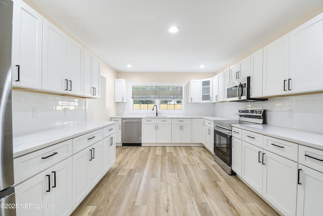 kitchen with a sink, appliances with stainless steel finishes, white cabinets, and light stone counters