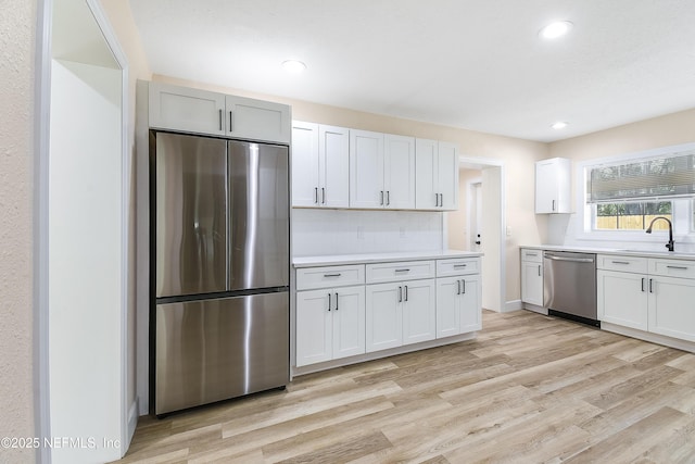 kitchen with light wood-style flooring, stainless steel appliances, a sink, white cabinetry, and light countertops