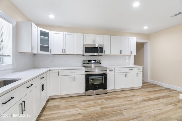 kitchen with visible vents, white cabinets, appliances with stainless steel finishes, light wood-type flooring, and glass insert cabinets