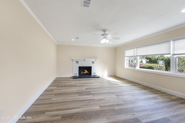 unfurnished living room with a lit fireplace, ornamental molding, visible vents, and baseboards