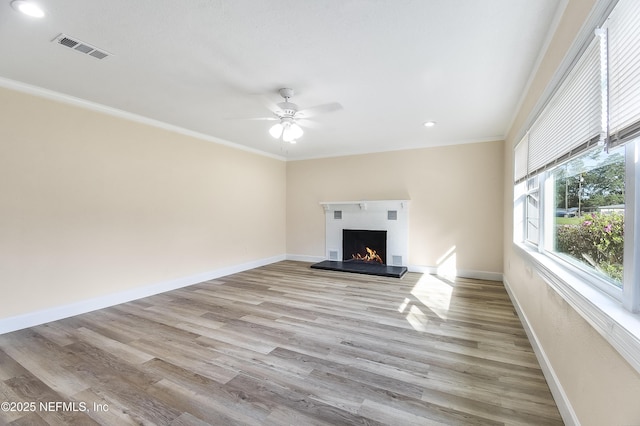 unfurnished living room featuring a warm lit fireplace, light wood-style floors, visible vents, and baseboards