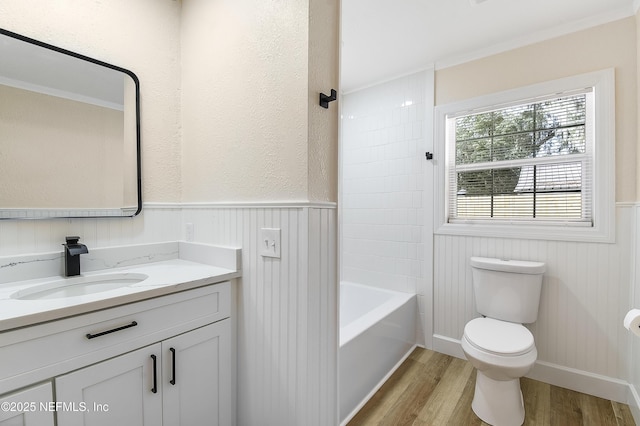 bathroom featuring wainscoting, toilet, wood finished floors, tub / shower combination, and vanity