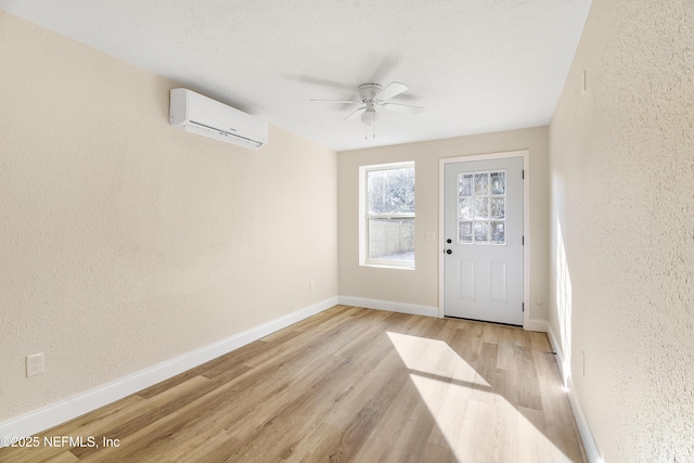 interior space featuring baseboards, a wall mounted air conditioner, a textured wall, and light wood finished floors