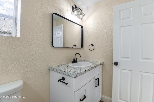 half bath featuring toilet, a textured wall, and vanity