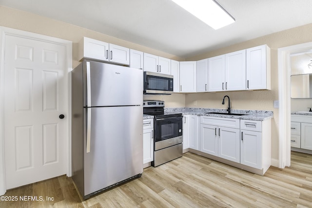 kitchen featuring stainless steel appliances, light wood finished floors, a sink, and white cabinets