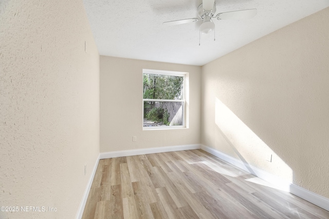 empty room with a textured wall, a ceiling fan, light wood-style flooring, and baseboards