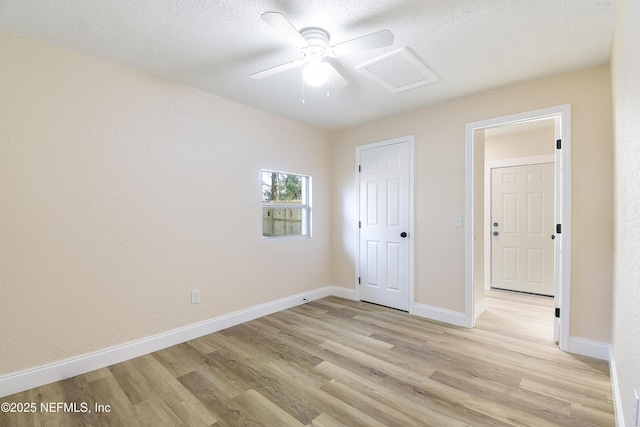 unfurnished bedroom with attic access, ceiling fan, a textured ceiling, light wood-type flooring, and baseboards