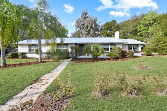 single story home with metal roof, a chimney, a front lawn, and stucco siding