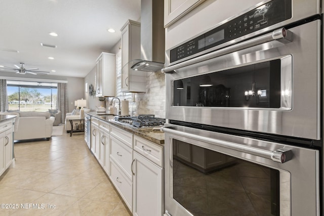 kitchen featuring decorative backsplash, appliances with stainless steel finishes, open floor plan, a sink, and wall chimney exhaust hood