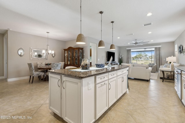 kitchen featuring dark stone counters, open floor plan, a center island with sink, and light tile patterned floors