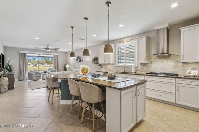 kitchen featuring stainless steel gas cooktop, a kitchen island, a sink, wall chimney range hood, and tasteful backsplash