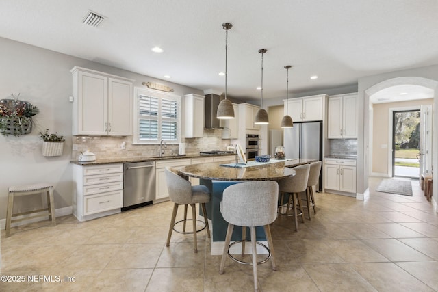 kitchen featuring arched walkways, a sink, visible vents, appliances with stainless steel finishes, and a kitchen bar