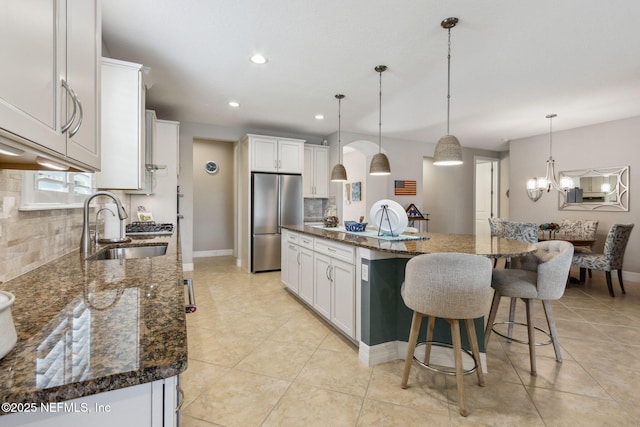 kitchen with a kitchen breakfast bar, white cabinets, a sink, and freestanding refrigerator