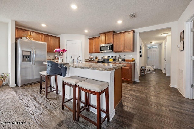 kitchen featuring appliances with stainless steel finishes, a breakfast bar area, brown cabinets, and an island with sink