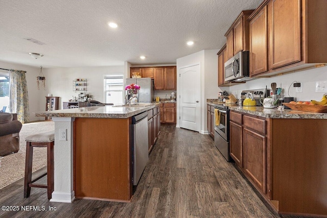 kitchen featuring stainless steel appliances, plenty of natural light, brown cabinetry, and a center island with sink