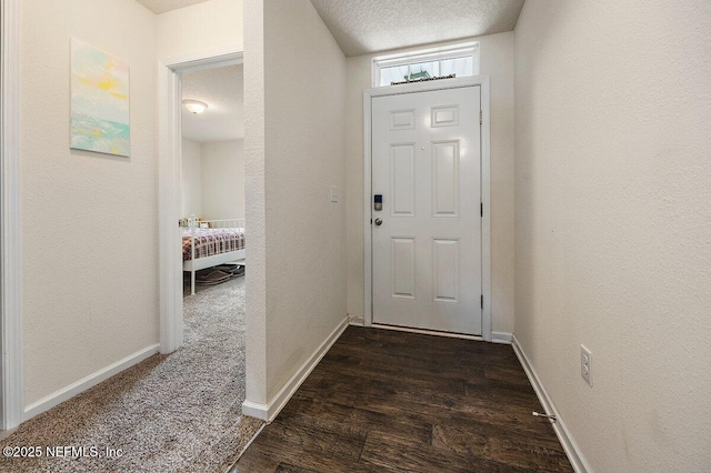 doorway to outside with a textured ceiling, a textured wall, dark wood-style flooring, and baseboards