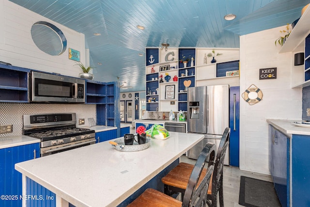 kitchen with blue cabinetry, stainless steel appliances, open shelves, and light countertops